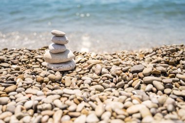 Çeşitli şekillerde, boyutlarda ve gölgelerde yuvarlak taşlardan oluşan bir piramit. Taşlar büyükten küçüğe üst üste konur. Fotoğrafta soldaki piramit var. Deniz, taşlar, gökyüzü