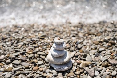 Çeşitli şekillerde, boyutlarda ve gölgelerde yuvarlak taşlardan oluşan bir piramit. Taşlar büyükten küçüğe üst üste konur. Tepesinde küçük bir kabuk var. Deniz, taşlar. Suyun parıltısı.