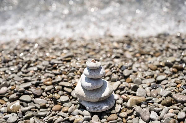 A pyramid of rounded stones of various shapes, sizes and shades. The stones lie one on top of the other from large to small. there is a small shell on top. Sea, stones. Glitter of water