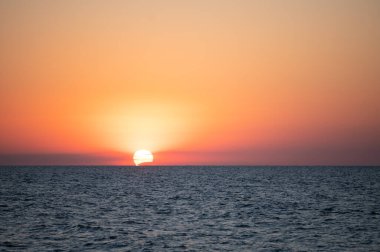 Denizde gün batımı. Güneş ufukta battı ve bulutların arkasında yavaşça kayboldu.. 