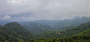 Mavi gökyüzünün altında büyük dağlar ve yeşil orman bulutlarla Trabzon 'da güzel bir manzara oluşturur.