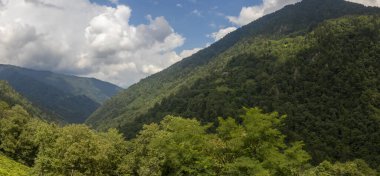 Mavi gökyüzünün altında büyük dağlar ve yeşil orman bulutlarla Trabzon 'da güzel bir manzara oluşturur.