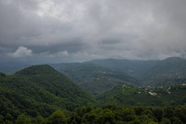Mavi gökyüzünün altında büyük dağlar ve yeşil orman bulutlarla Trabzon 'da güzel bir manzara oluşturur.