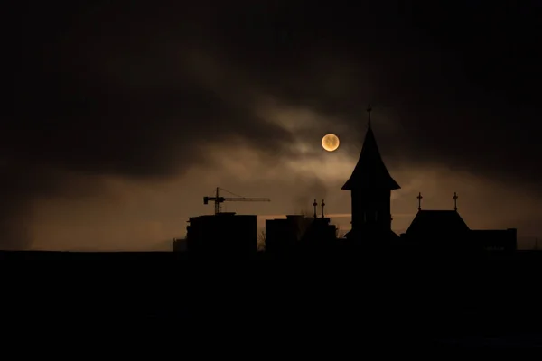 Sis ve karanlık gökyüzü ile gün doğumunu siluet kilise ve bina inşaatı ile karartır.