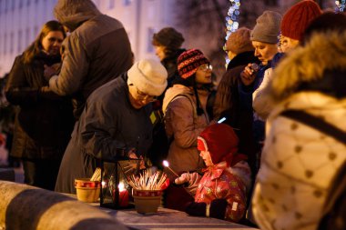 Tartu, Estonya - 11 Aralık 2016: Noel geleneği: Advent akşam Town Hall Meydanı'nda kutsal ateşten ışık mumlar insanlar. Uzun bir maç ile bir çocuk ateşin önünde görünüyor.