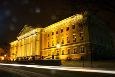 Bir kış akşamı Noel dekor Tartu Üniversitesi ana binanın cephe. Arabanın ön planda izleme.