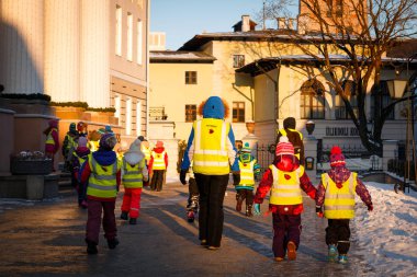 Tartu, Estonya - 11 Ocak 2017: Tartu Üniversitesi yakınındaki eski şehirde bir yolda çocuklu bir anaokulu öğretmeni. Çocuk güvenliği için yansıtıcı yelek giymiş.