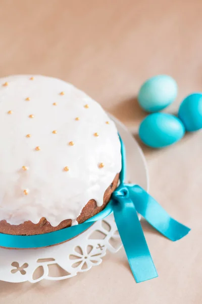 Traditional Easter cake with frosting, blue ribbon and golden balls decoration and blue colored eggs on the craft paper background