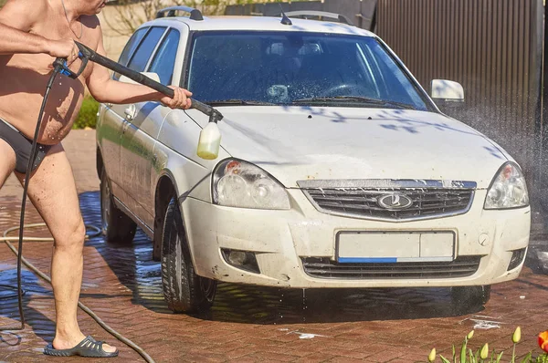 Bir adam sokakta karanlık Yüzme şort beyaz bir araba yıkar