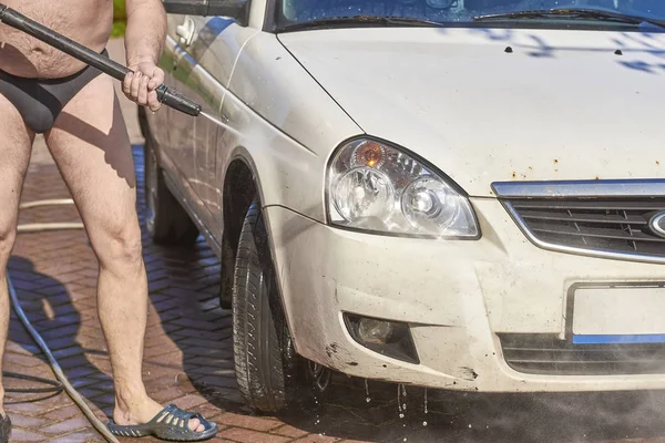 Un hombre en traje de baño oscuro en la calle lava un coche blanco — Foto de Stock