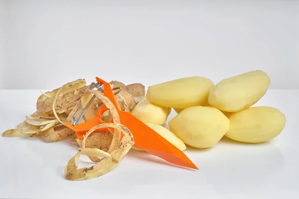 Patate crude pelate, patate pelate e un pelapatate su una ba bianca — Foto Stock