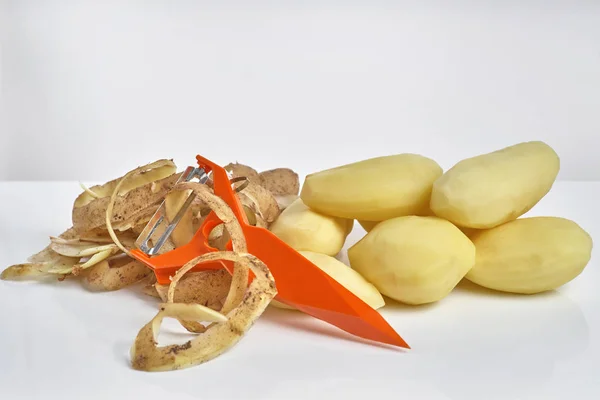 Batatas cruas descascadas, batatas descascadas e um descascador em uma ba branca — Fotografia de Stock