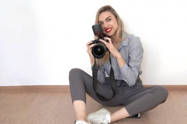 Genç, seksi sarışın stüdyoda yerde oturuyor ve elinde bir silah tutuyor.