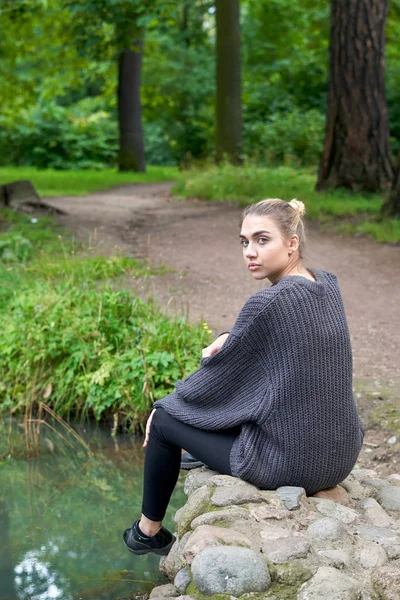 Una giovane ragazza siede sulle pietre vicino a un lago di foresta — Foto Stock