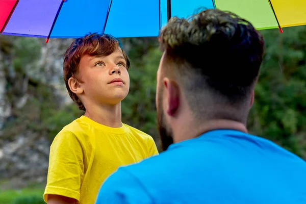 Día de los padres al aire libre. Padre e hijo bajo un color arcoíris umbrel Imagen De Stock