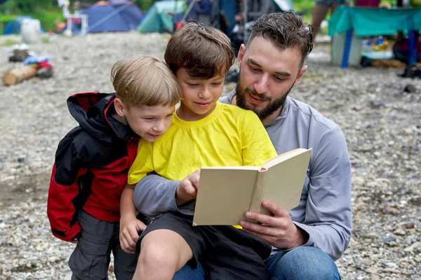 Un père lit un livre à ses deux fils en campant — Photo