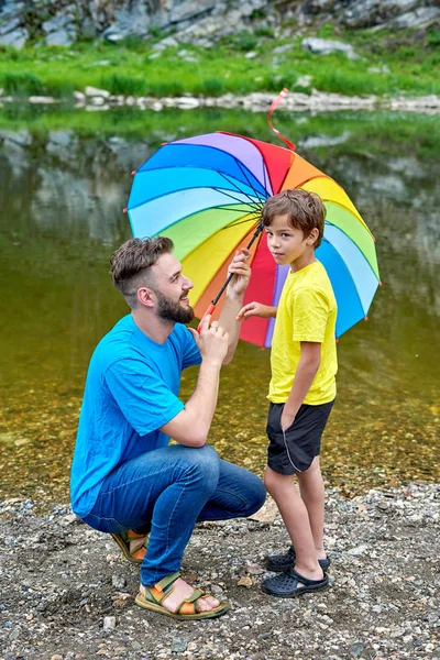 Día de los padres al aire libre. Padre e hijo bajo un color arcoíris umbrel Fotos De Stock