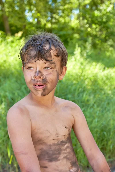 El niño untó la cara, las manos y el cuerpo en el barro . Imagen De Stock