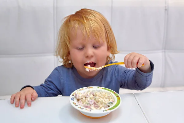 Un bambino di tre anni a un tavolo mangia l'insalata da un piatto — Foto Stock