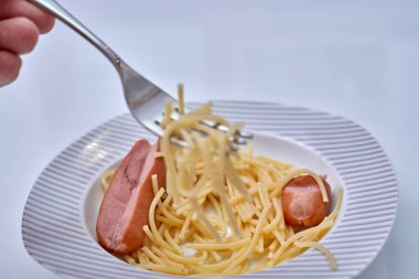 Beyaz tabakta makarnalı sosisler, beyaz arka planda yakın plan.