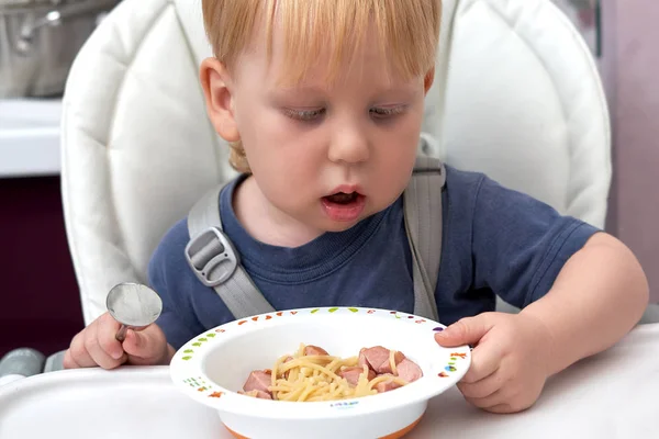 Un garçon de trois ans mange dans une assiette avec une cuillère — Photo