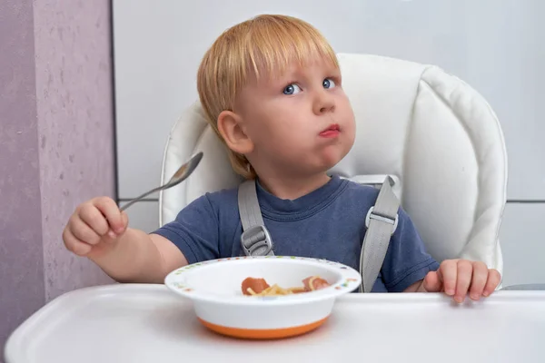 Un garçon de trois ans mange dans une assiette avec une cuillère — Photo