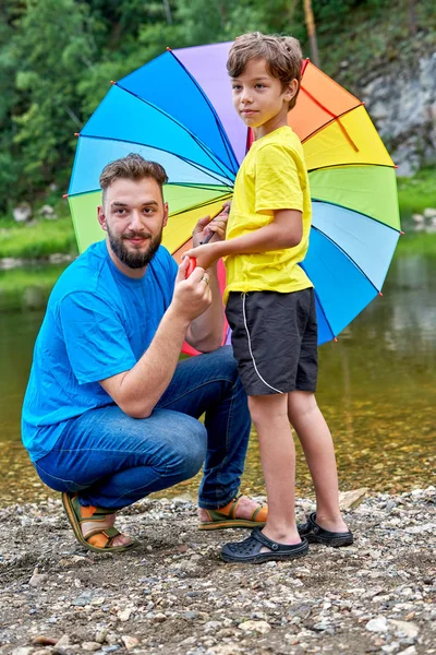 Día de los padres al aire libre. Padre e hijo bajo un color arcoíris umbrel Imágenes De Stock Sin Royalties Gratis