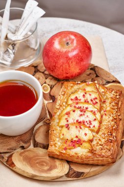 Taze meyveli turta, bir fincan çay ve arka planda kırmızı elmalarla dolu bir hayat. Yakın çekim, dikey çekim