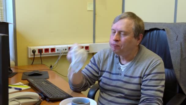 De man in het kantoor eet, veegt zijn mond af met een medisch masker, en gooit het dan weg. — Stockvideo