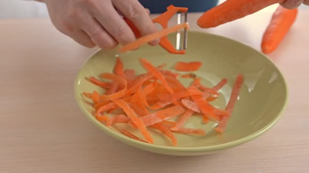 Ręce trzymające pomarańczowe czyszczenie warzyw i obieranie czerwonej marchewki w zielonej misce — Wideo stockowe