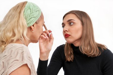 Kız arkadaşına makyaj uygular. Kozmetik kalemle göz kalemi. Esmer, sarıya boyar. Beyaz arkaplanda izole et