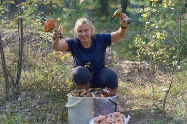 Kız mantar kovalarının önünde oturuyor. Sarışın elinde büyük bir boletus tutuyor.