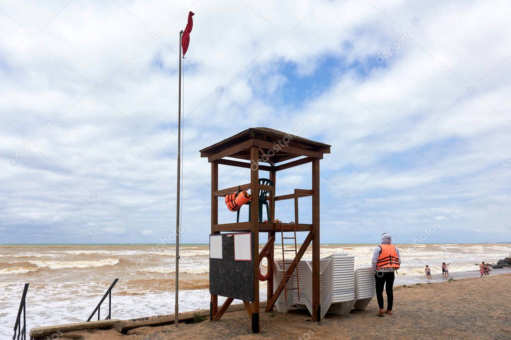 Rescue tower and lifeguard in an orange vest on the shore during a storm. Empty beach at the end of the holiday season