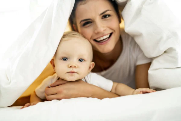 Portré fiatal anya a csecsemő baba lány liying az ágyon a fehér takaró fedi — Stock Fotó