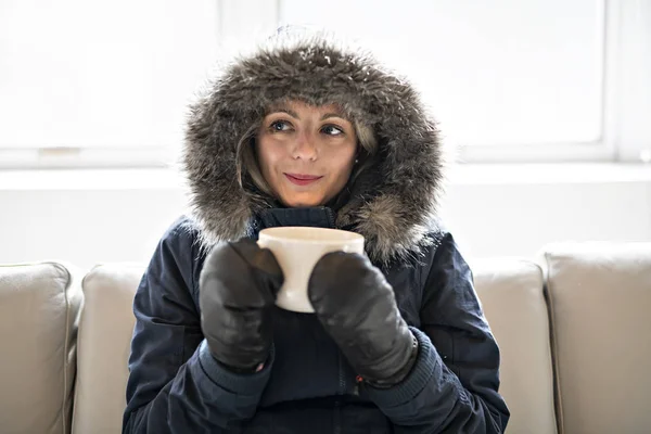 Femme ont café boisson froide sur le canapé à la maison avec manteau d'hiver — Photo