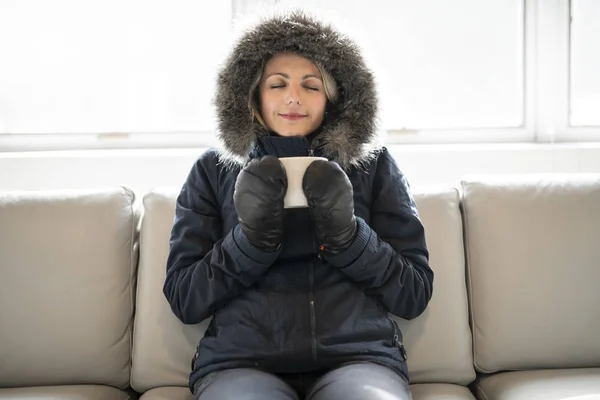 Femme ont café boisson froide sur le canapé à la maison avec manteau d'hiver — Photo