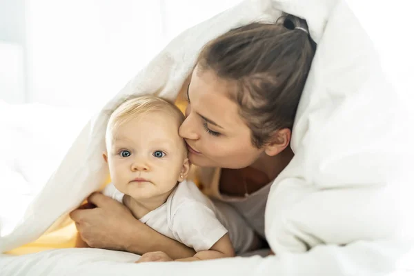 Retrato de jovem mãe com bebê menina deitada na cama coberta com um cobertor branco — Fotografia de Stock