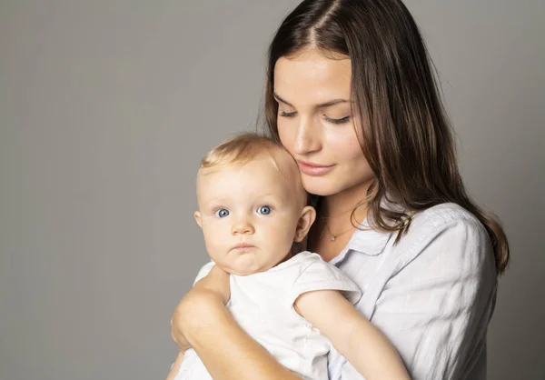Una madre tiene il suo bambino su sfondo grigio studio — Foto Stock