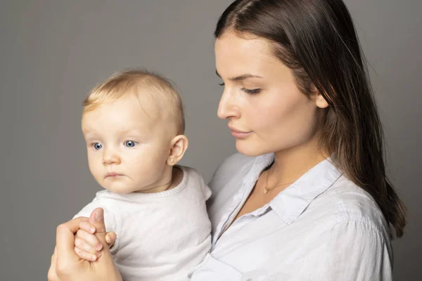 Una madre tiene il suo bambino su sfondo grigio studio — Foto Stock