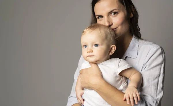 Una madre tiene il suo bambino su sfondo grigio studio — Foto Stock