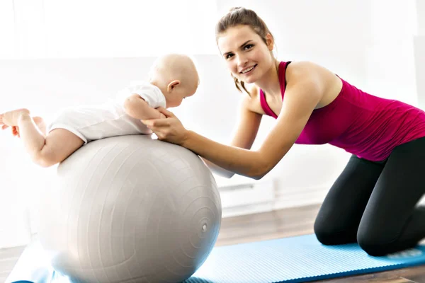 Un retrato de una hermosa madre joven en ropa deportiva con su encantador bebé en sesión de entrenamiento — Foto de Stock