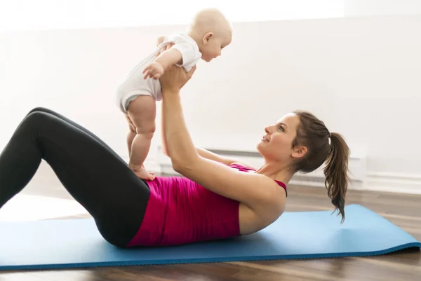 A Portrait of beautiful young mother in sports wear with her charming little baby in training session — Stock Photo, Image