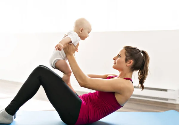 Un retrato de una hermosa madre joven en ropa deportiva con su encantador bebé en sesión de entrenamiento — Foto de Stock