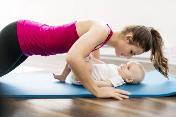 Un retrato de una hermosa madre joven en ropa deportiva con su encantador bebé en sesión de entrenamiento — Foto de Stock