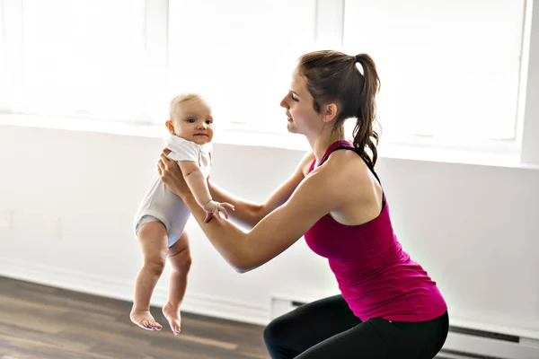 Un retrato de una hermosa madre joven en ropa deportiva con su encantador bebé en sesión de entrenamiento — Foto de Stock