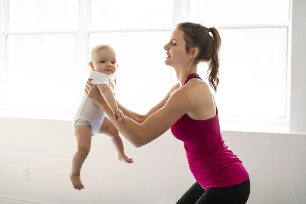 Um retrato de bela jovem mãe em roupas esportivas com seu pequeno bebê encantador em sessão de treinamento — Fotografia de Stock