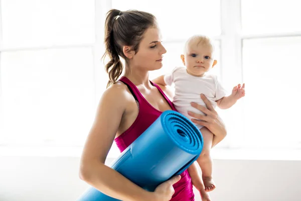 Portrét krásné mladé matky v oblasti sportovního oblečení s její okouzlující malé dítě v tréninku — Stock fotografie