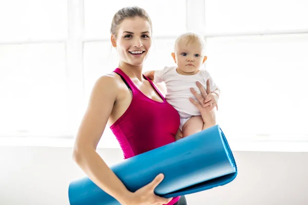 Portrét krásné mladé matky v oblasti sportovního oblečení s její okouzlující malé dítě v tréninku — Stock fotografie
