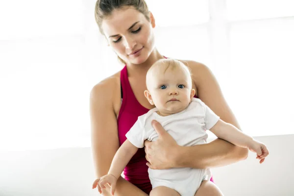 A Portrait of beautiful young mother in sports wear with her charming little baby in training session — Stock Photo, Image
