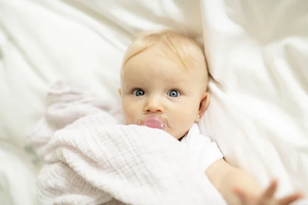 Un bambino carino con ciuccio sdraiato su un letto bianco — Foto Stock